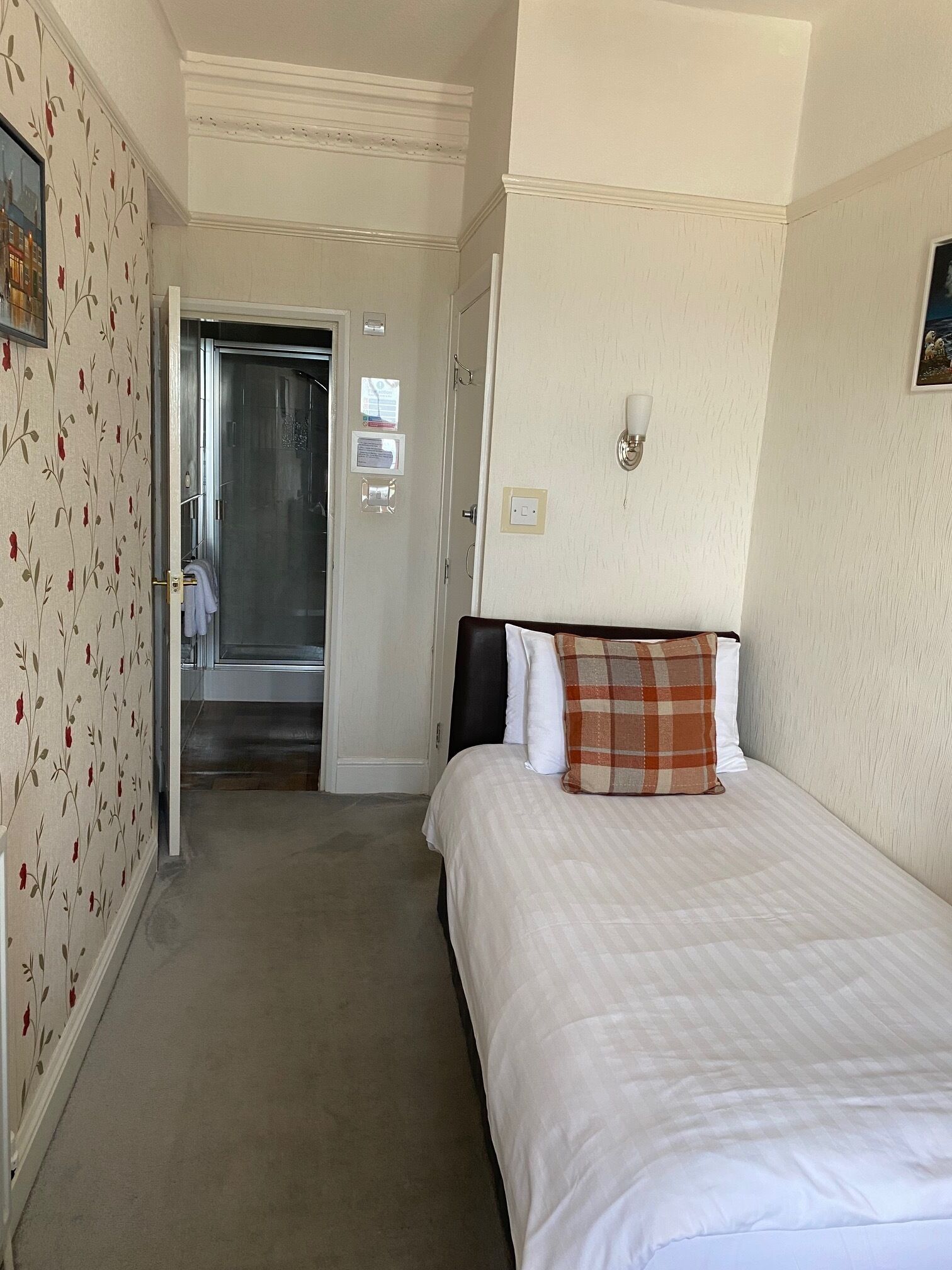 A hotel room with a bed, a door leading to a bathroom, and a wall-mounted light fixture.