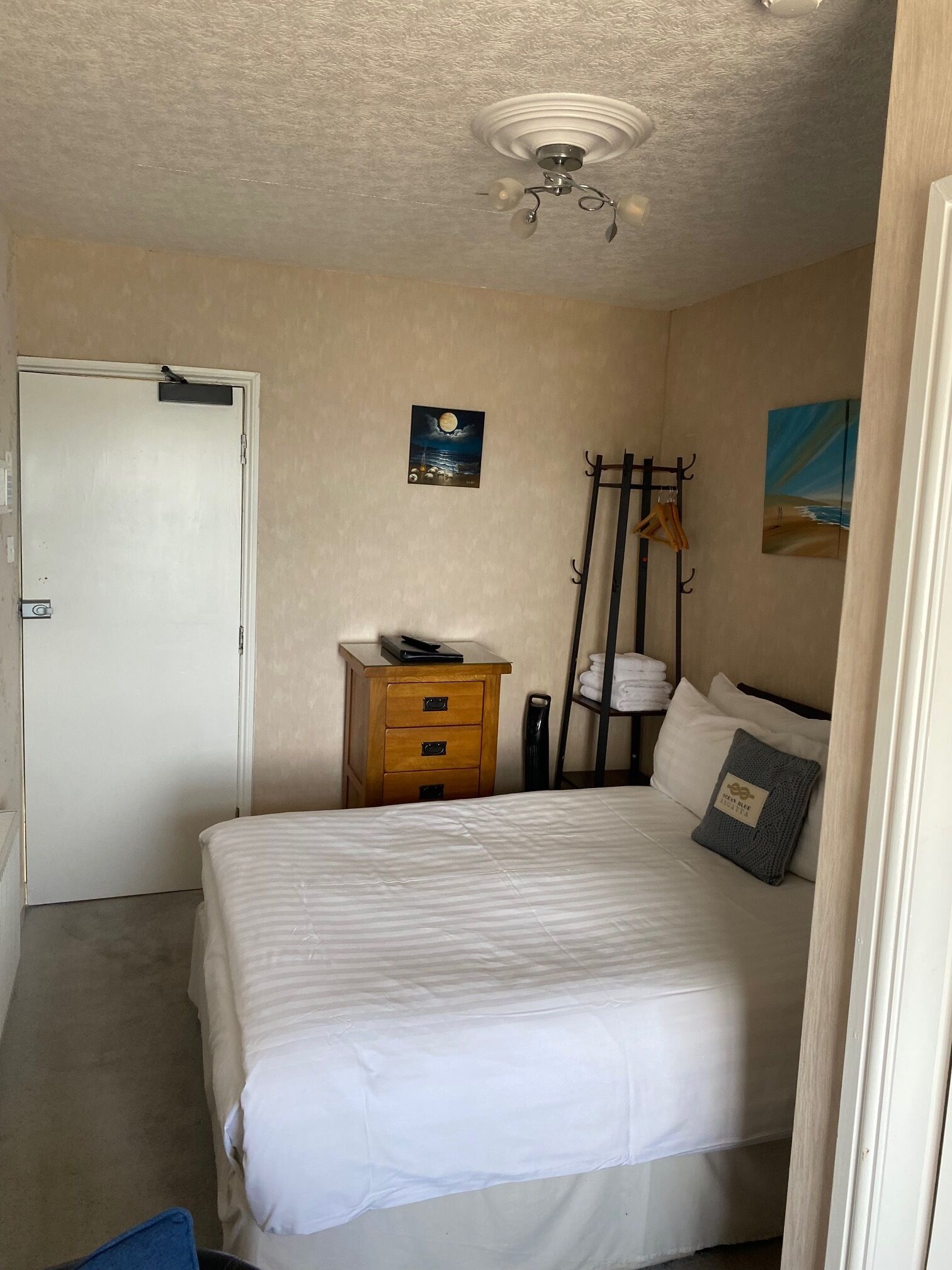 A bedroom with a bed, a nightstand, a coat rack, and a door.