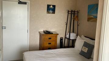 A bedroom with a bed, a nightstand, a coat rack, and a door.