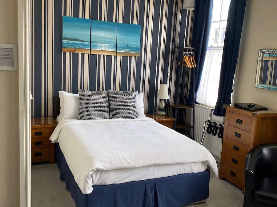 A bedroom with a bed, a ceiling fan, a window with curtains, and a painting on the wall.