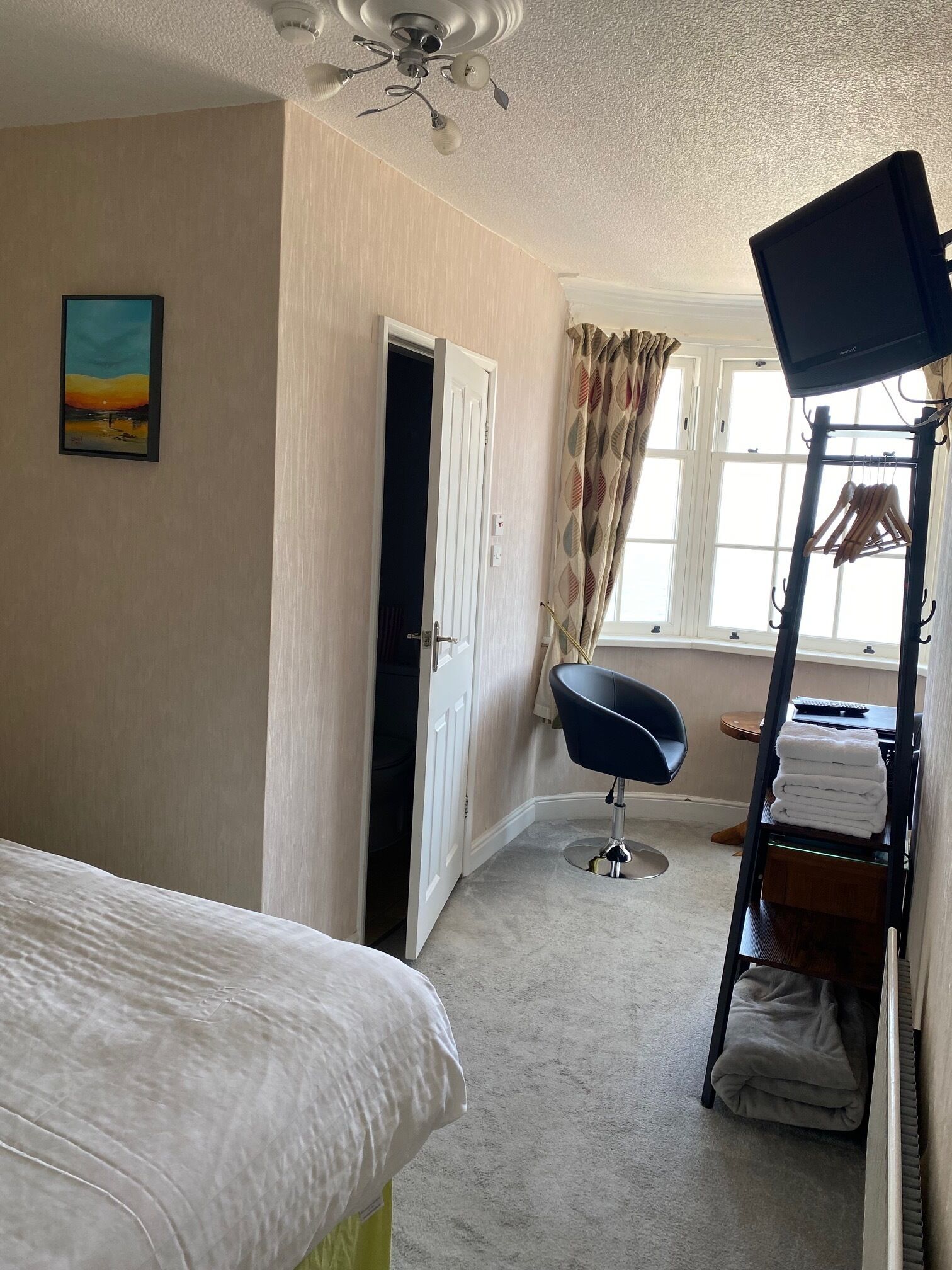 Un dormitorio con cama, una silla, armario, ventilador de techo y ventana con cortinas.