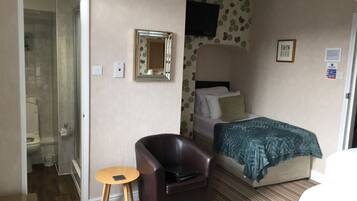A hotel room with a bed, a chair, a small table, a mirror, and a shower area.