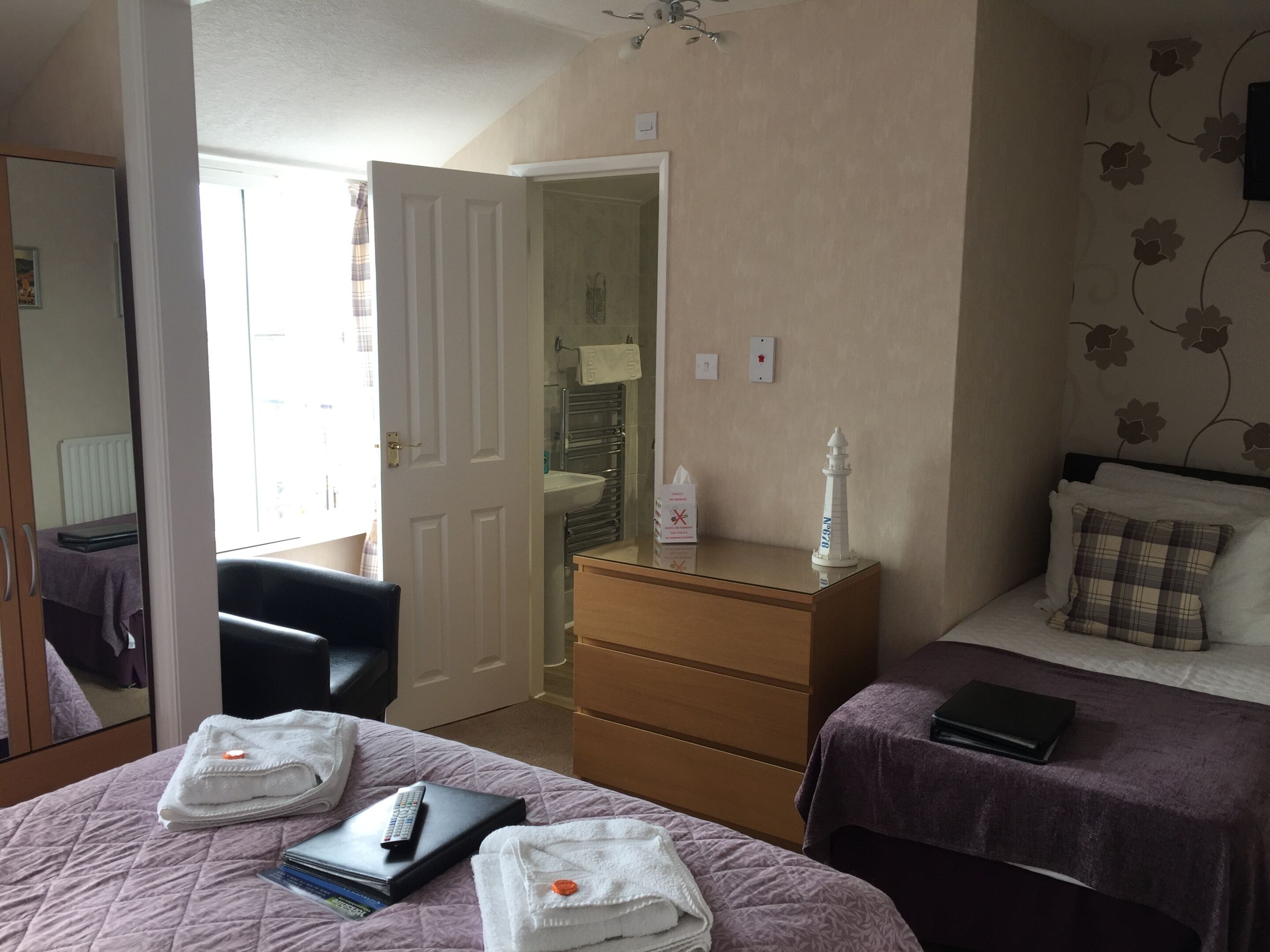 A bedroom with two beds, a dresser, a chair, and a small table with a lamp.