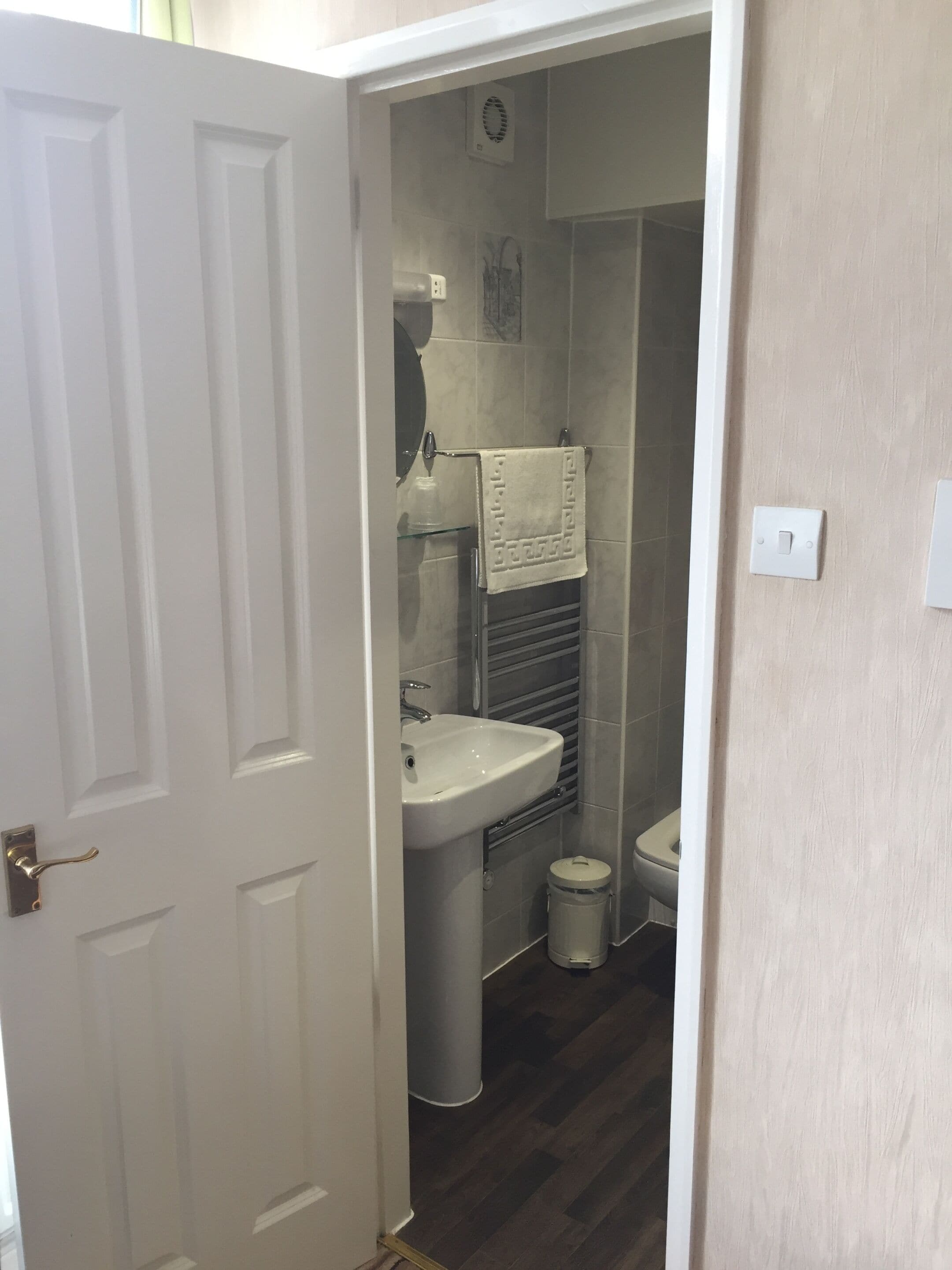 A small, narrow bathroom with a white door, a sink, a toilet, and a towel hanging on a rack.