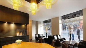 A modern hotel lobby with a large wooden table, leather seating, and a fireplace. - Citiz Hotel (Toulouse)