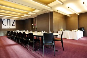 Un salón de conferencias en el hotel CITIZEN, con una larga mesa dispuesta para reuniones, sillas negras y un mantel blanco.