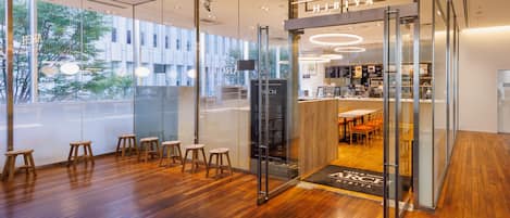 Un café moderne avec une façade en verre, un plancher en bois et un espace salon bien visible, équipé de tabourets.