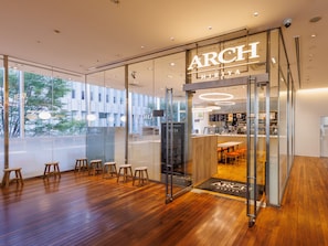 A modern cafe with a glass facade, wooden flooring, and a visible seating area with stools.