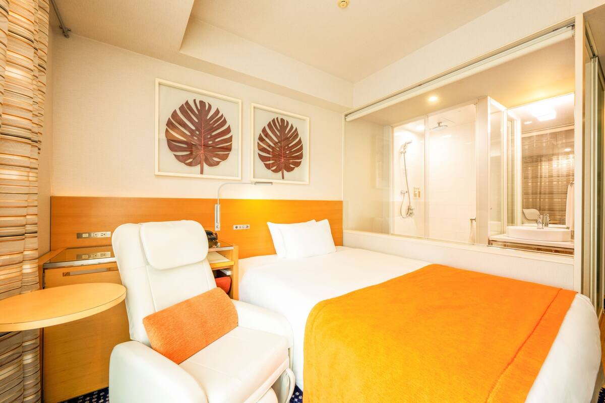 A hotel room with two beds, a sitting area, a shower, and artwork on the wall.
