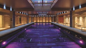 Une piscine intérieure moderne dotée d’un élément aquatique central, de puits de lumière et d’espaces de détente le long des parois.