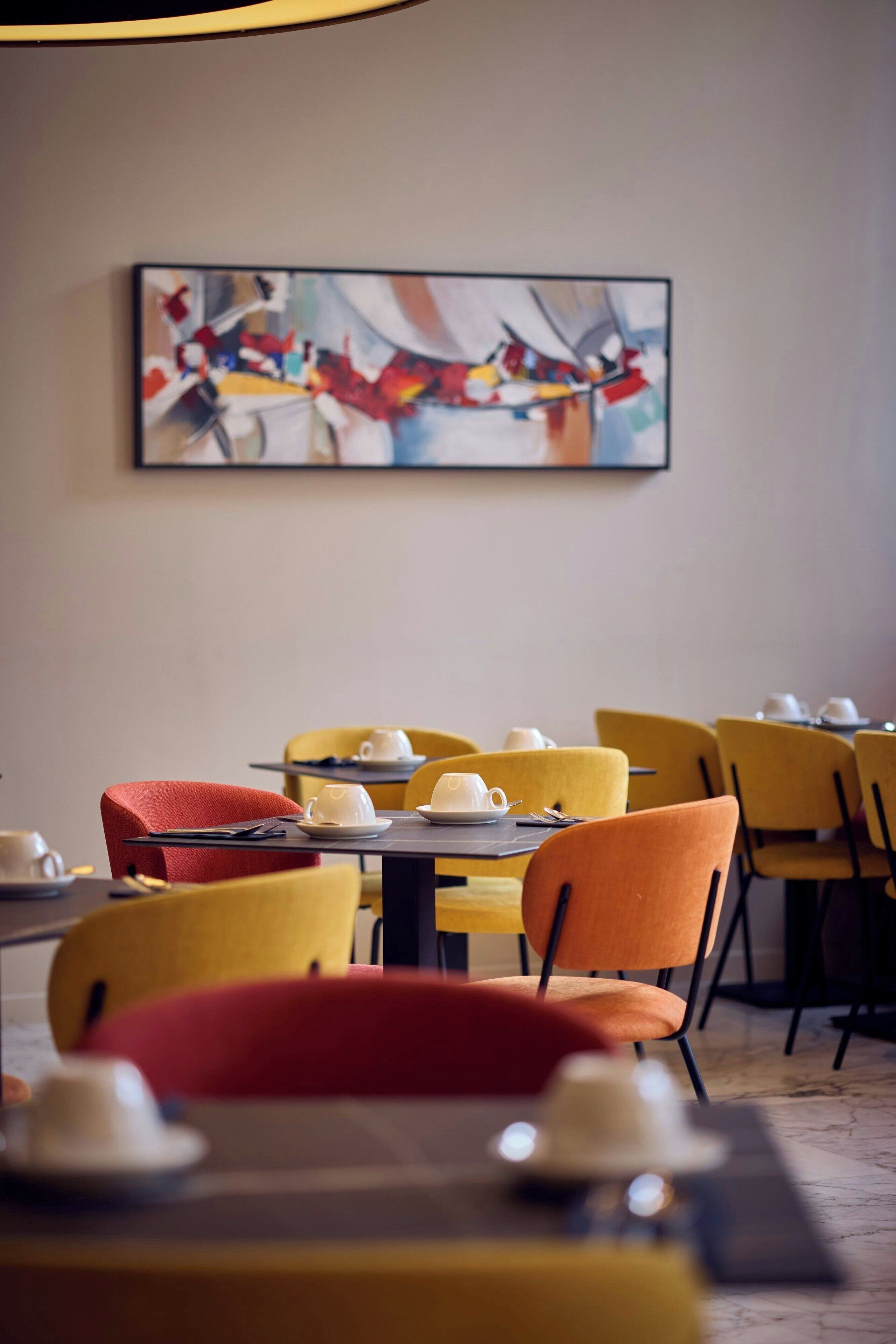 A dining area with tables set for service, chairs in various colors, and a painting on the wall.