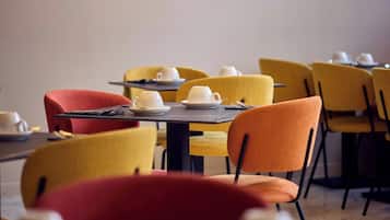 A dining area with tables set for service, chairs in various colors, and a painting on the wall.