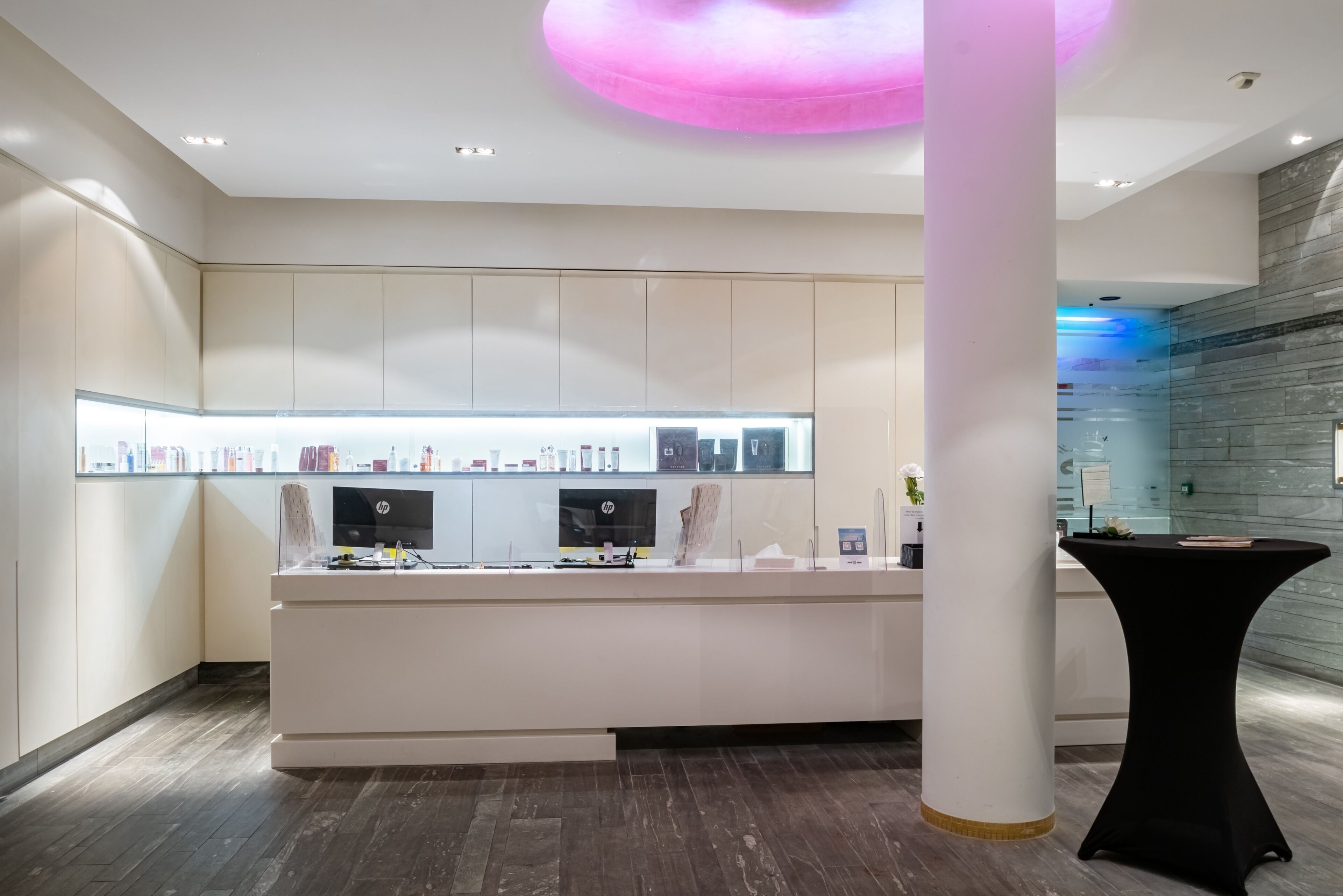 Un espace d’accueil avec un comptoir blanc, deux écrans et une vitrine.