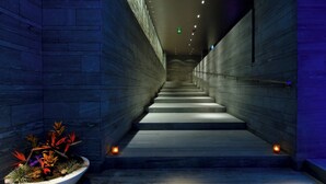 Un escalier moderne au design minimaliste, flanqué de murs en pierre sombre et agrémenté d’une plante en pot à sa base.