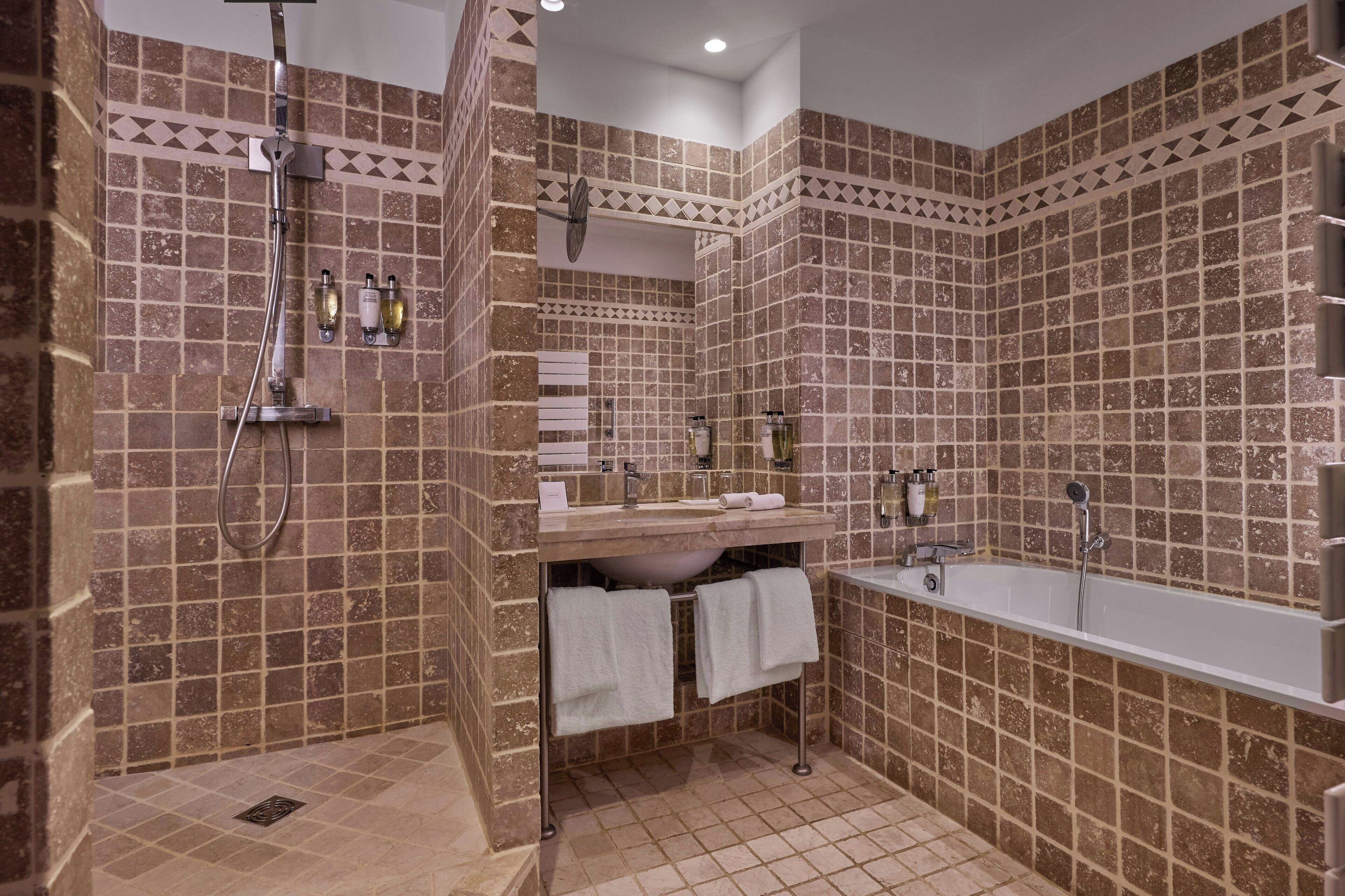 Un bagno con doccia, lavandino e vasca, rivestito di piastrelle marroni con un motivo geometrico.