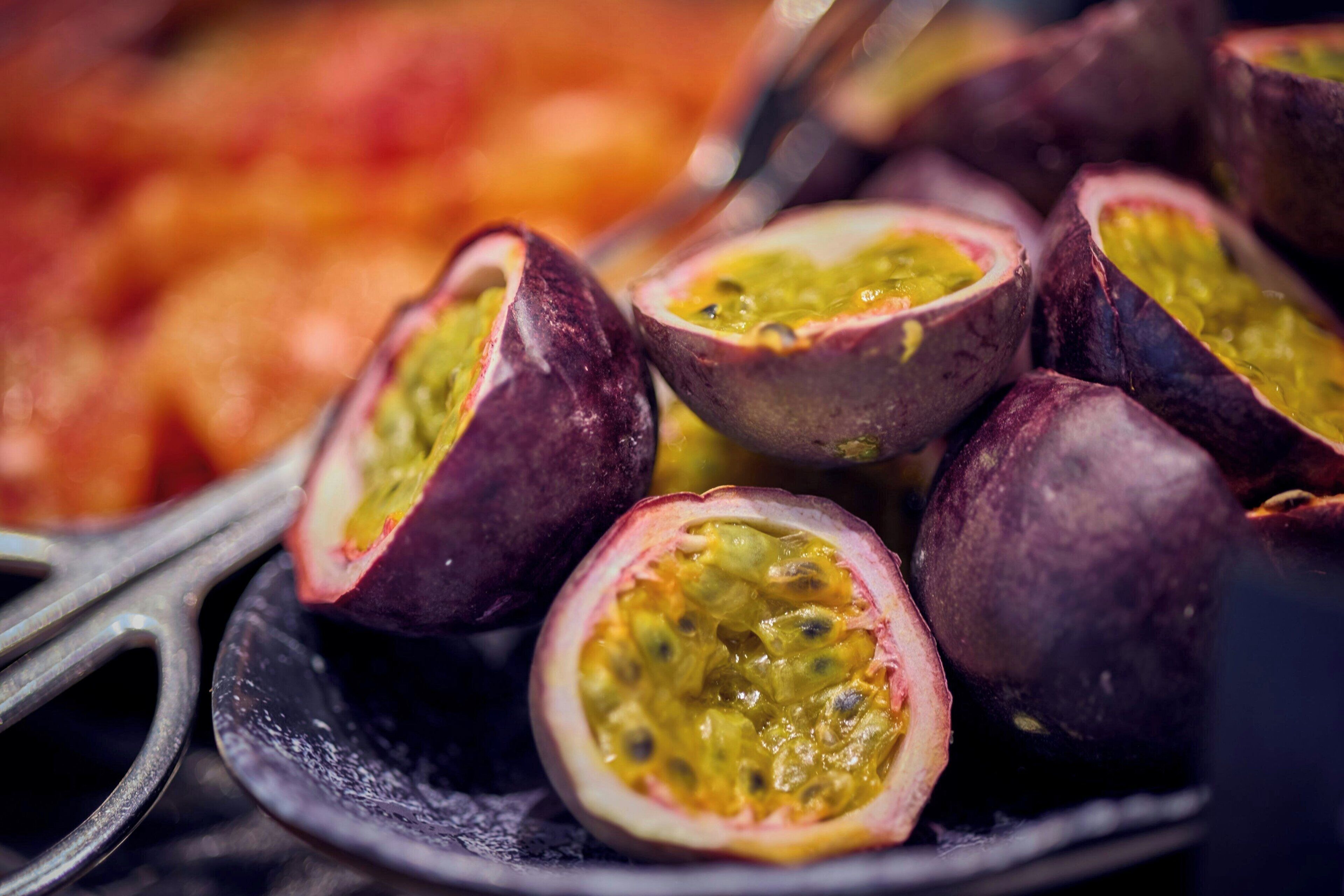 Primer plano de mitades de maracuyá con piel morada oscura y pulpa amarilla, dispuestas sobre un plato.