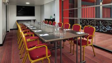 A conference room with a long table, red and yellow chairs, and a large screen on the wall.