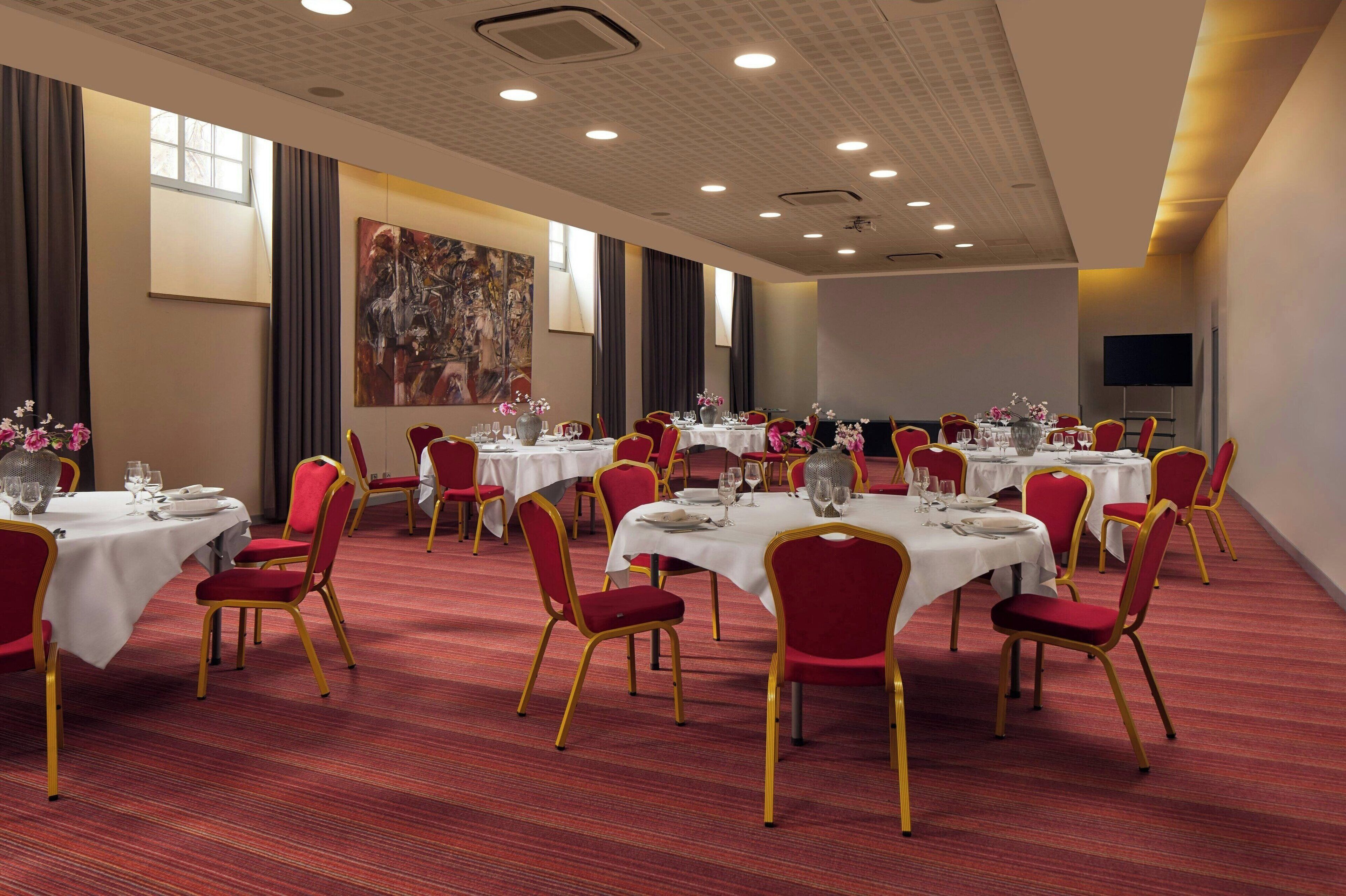 A conference room with tables set for a meeting, equipped with chairs, tables, and a large screen.