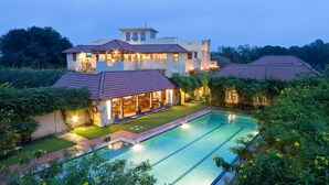 Una casa grande y luminosa con piscina, rodeada de vegetación.