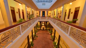 Un interior de varios niveles con una escalera central, columnas y plantas en macetas.