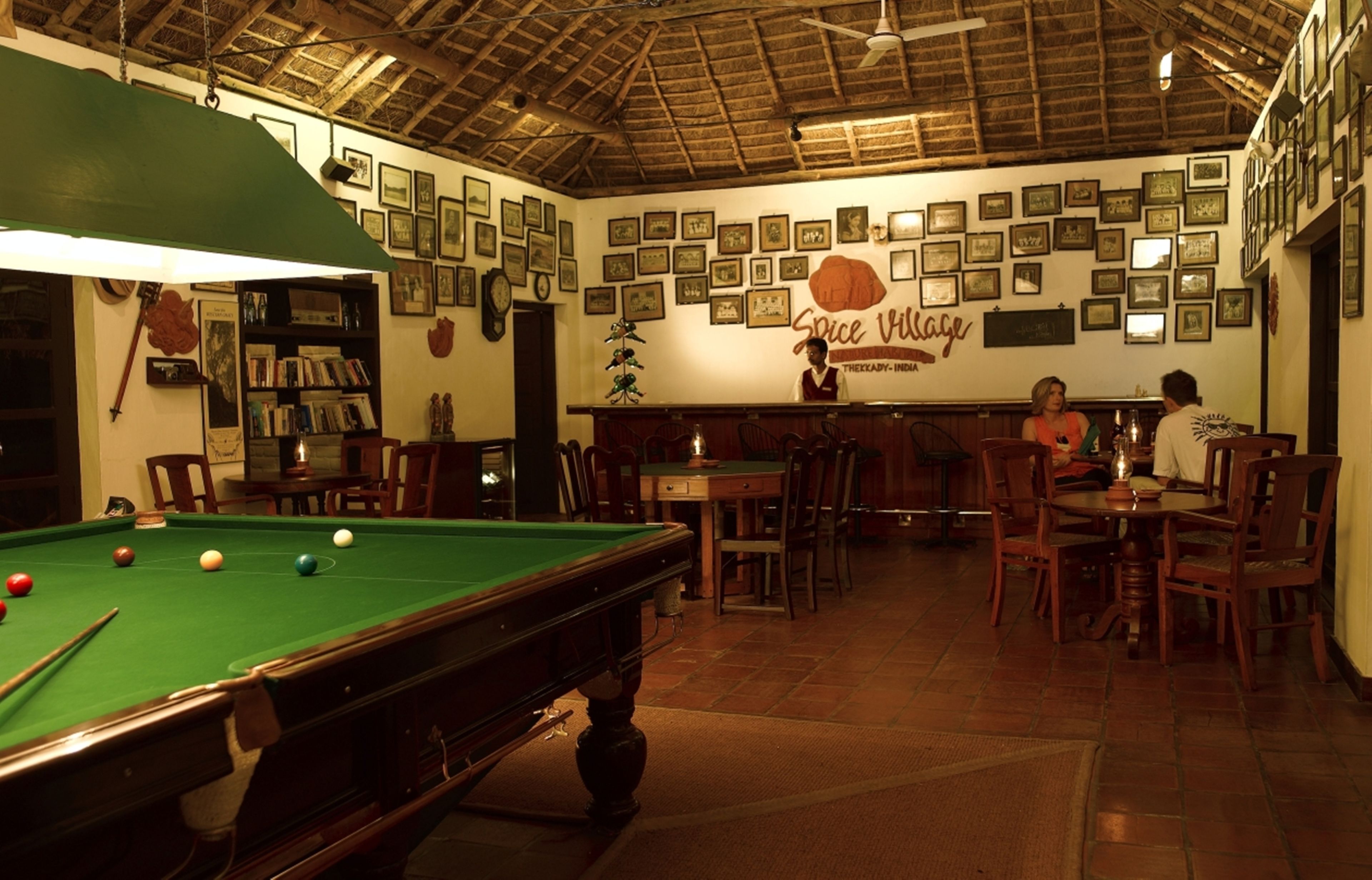 A billiards room with a pool table, chairs, and a wall decorated with framed pictures.