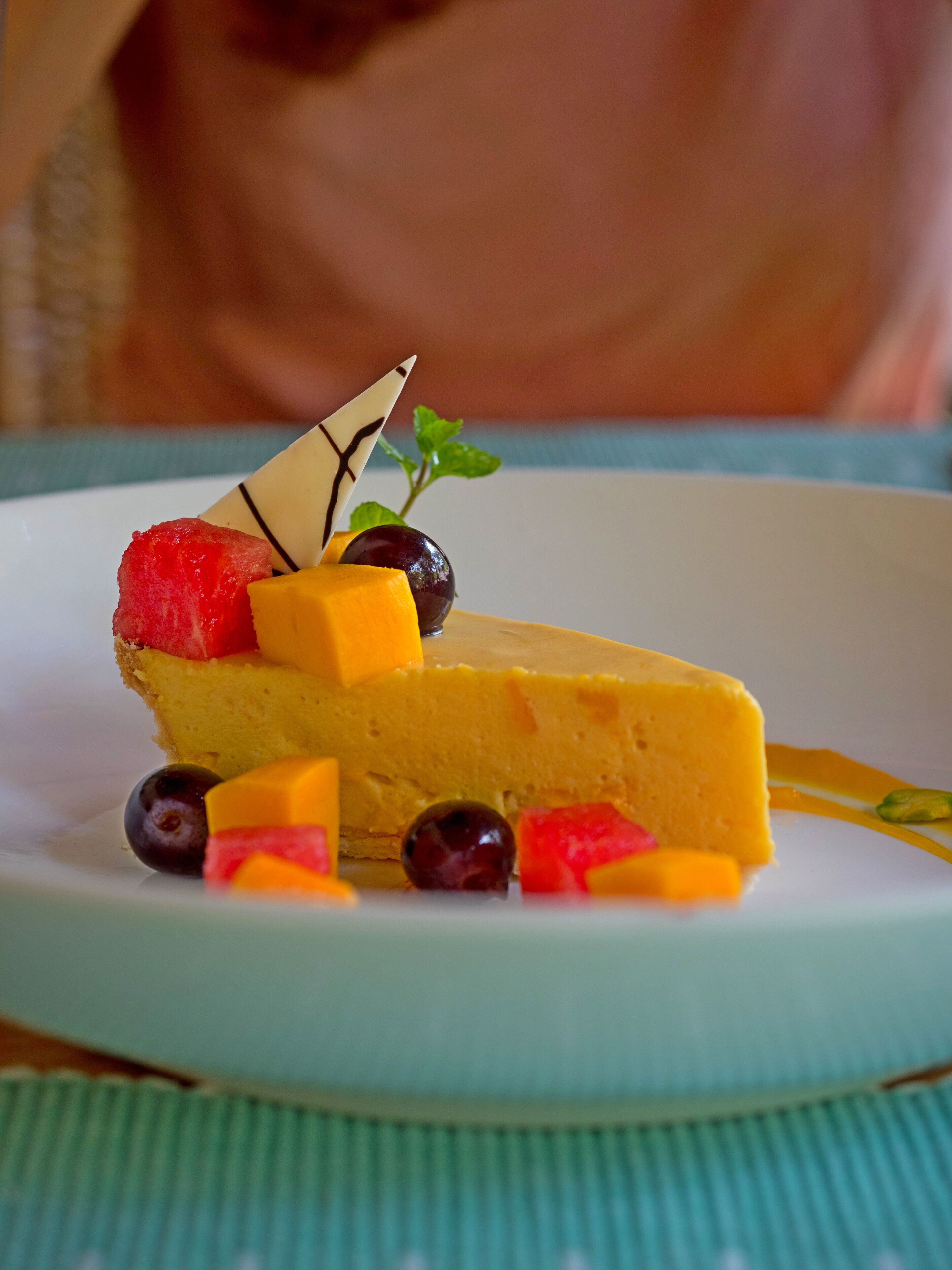 A slice of cheesecake on a white plate with fruit and chocolate garnish.