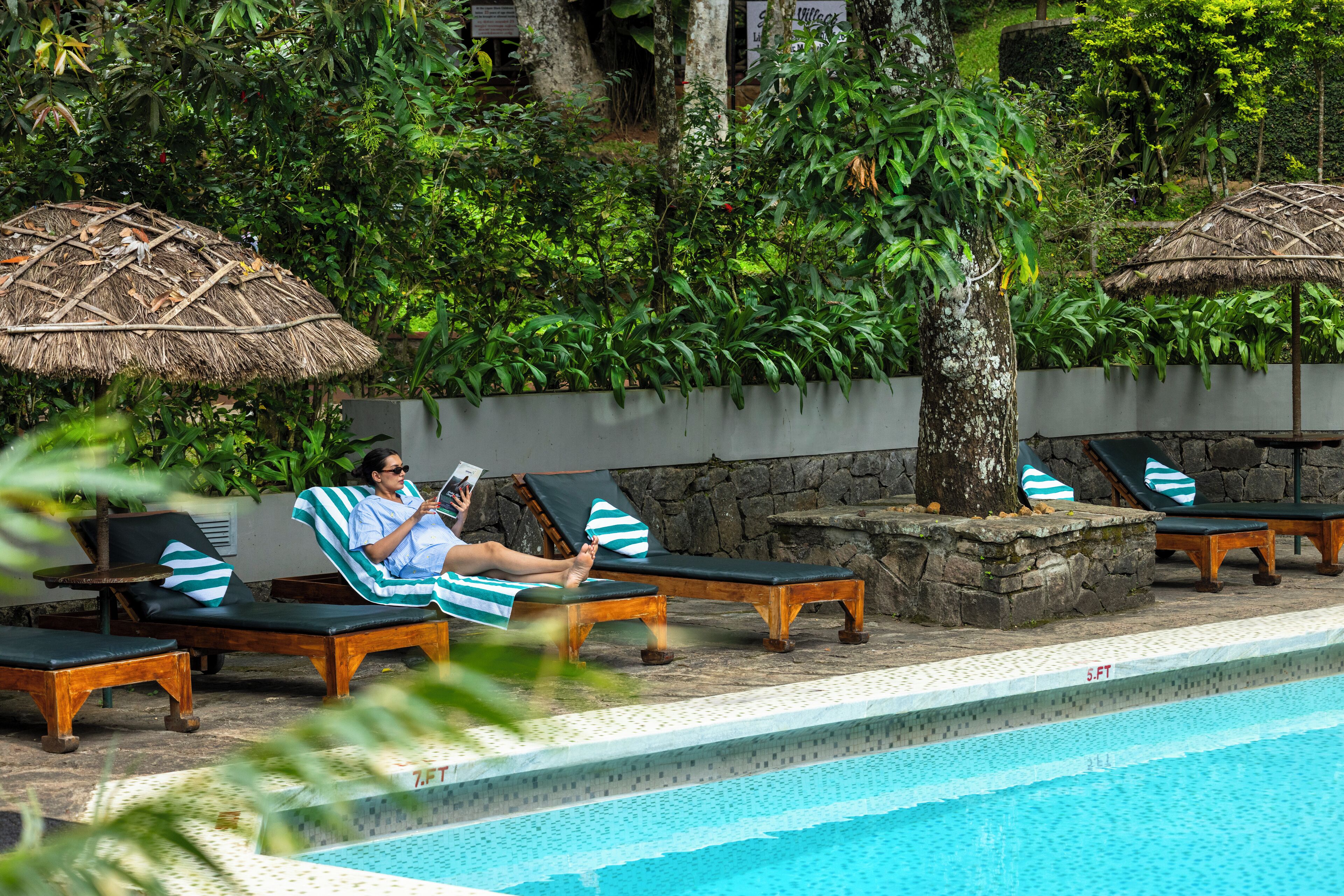 A poolside area with lounge chairs and umbrellas, surrounded by lush greenery.