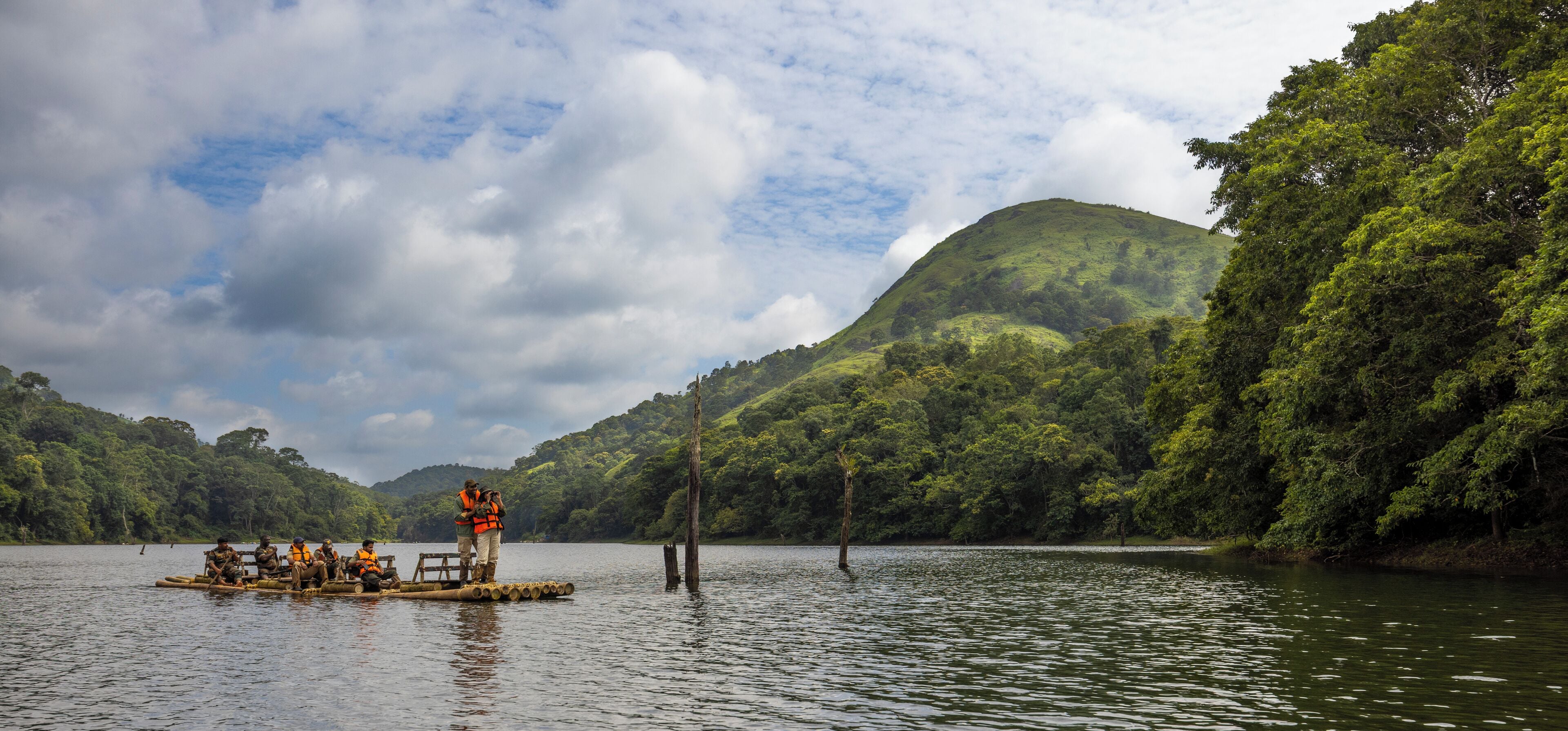 A group of people on a floating platform in a lake surrounded by lush greenery and hills.