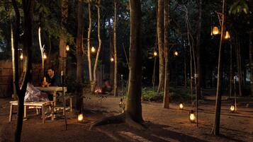 A rustic outdoor setting with wooden furniture and hanging lanterns, suggesting a campsite or outdoor dining area.