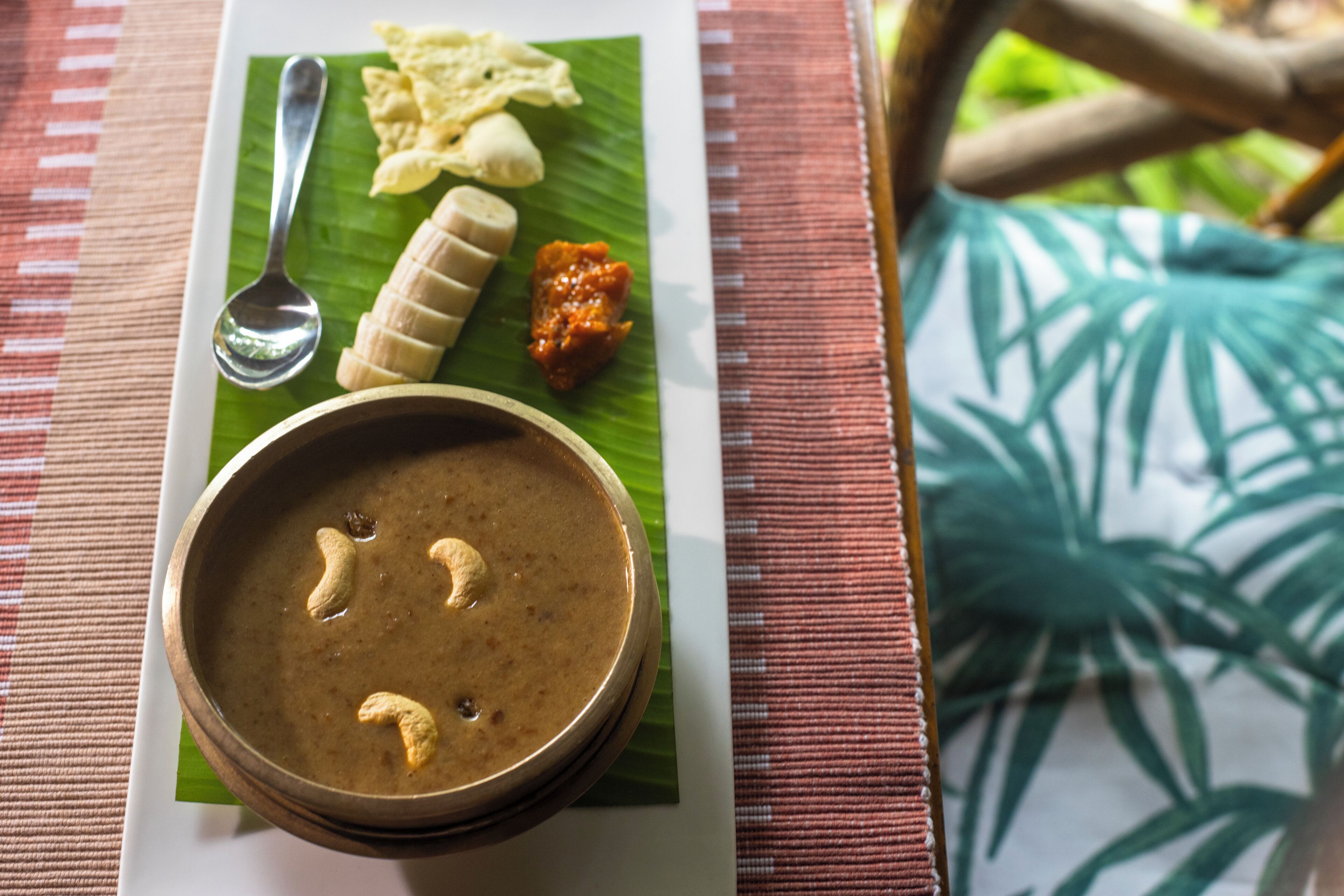 A meal served on a banana leaf with a bowl of soup, banana slices, and a small dish of sauce.