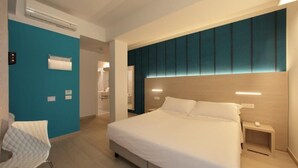 Habitación de hotel moderna con una cama grande, una mesita de noche, una silla y un baño visible a través de una puerta abierta.