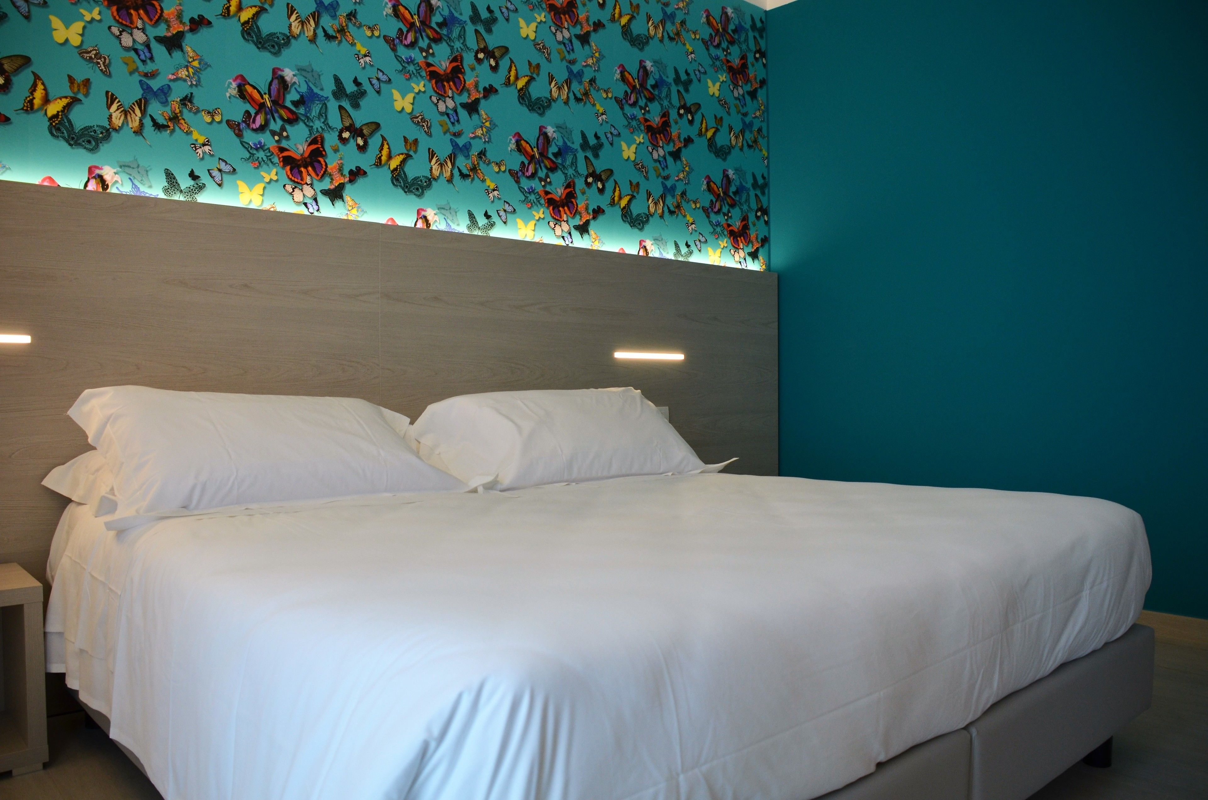A bed with white linens, a wooden headboard, and a wall with butterfly decals.