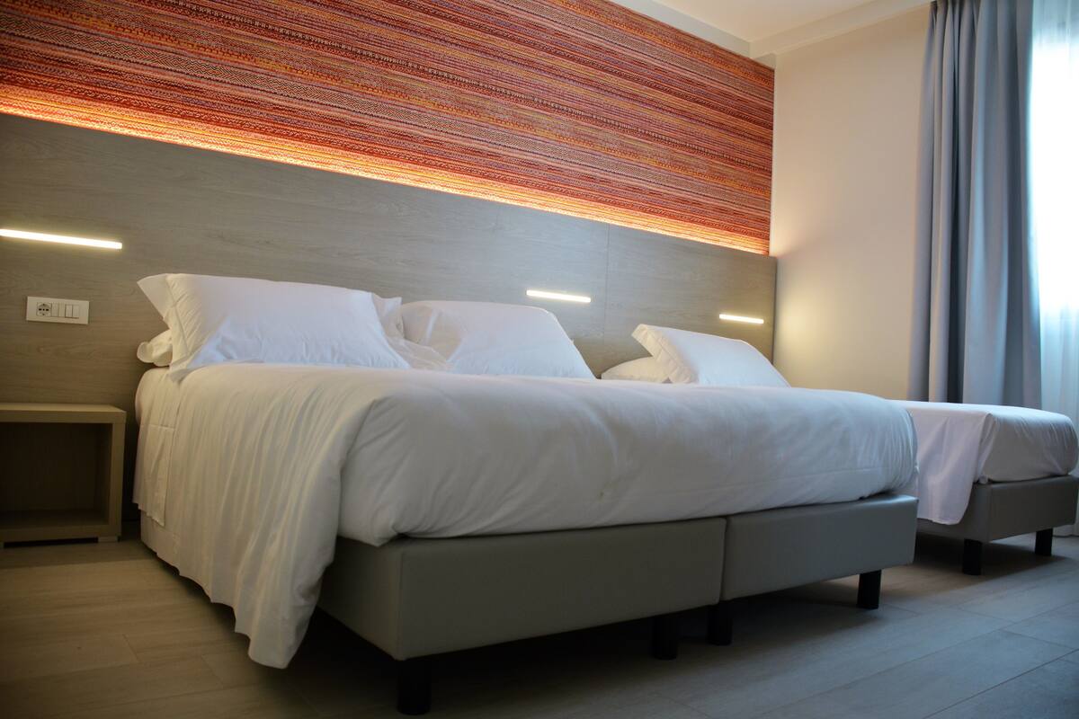 A modern bedroom with a large bed, bedside tables, and a patterned wall above.