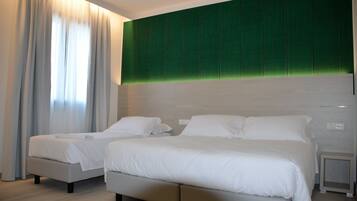 A modern hotel room with two beds, a green accent wall, and a large window with curtains.