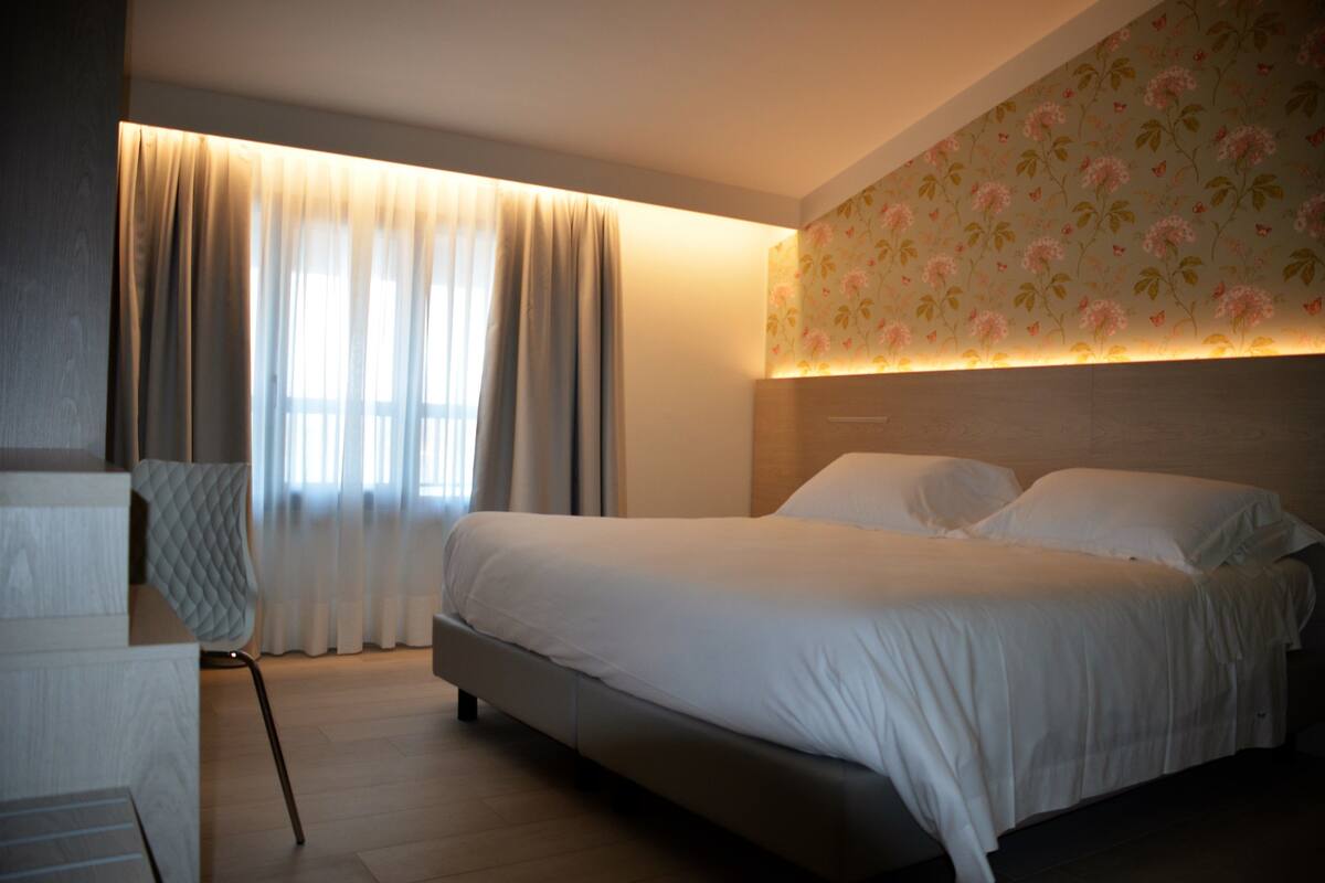 A modern bedroom with a large bed, a chair, and a window with curtains.