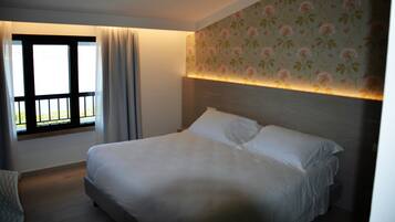 Une chambre d’hôtel avec un grand lit, une fenêtre avec des rideaux et un papier peint à motifs floraux.