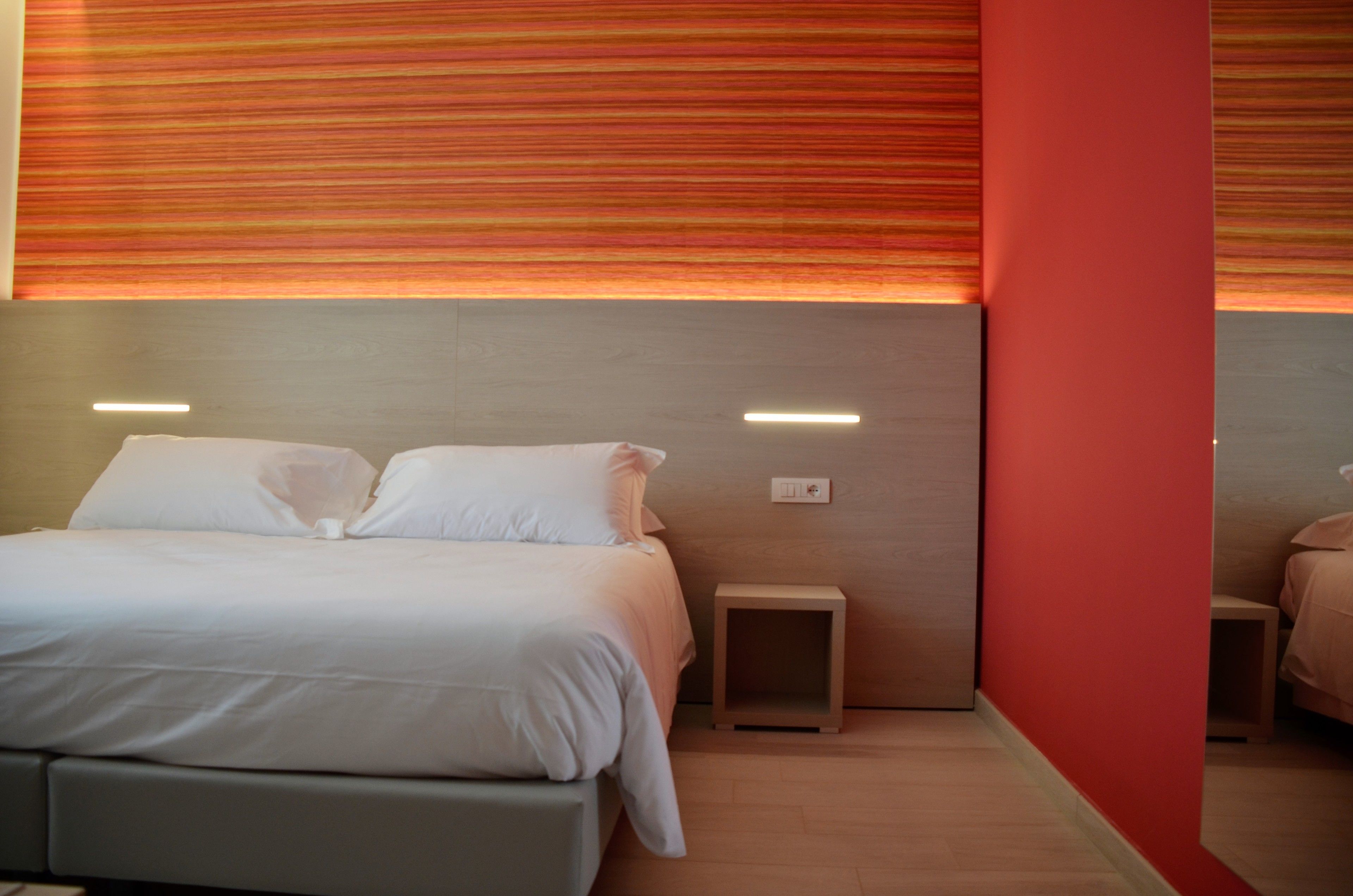 A modern hotel room with a large bed, bedside tables, and a red accent wall.