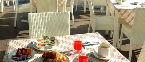 An outdoor café with tables and chairs, breakfast items, and a view of the sea.