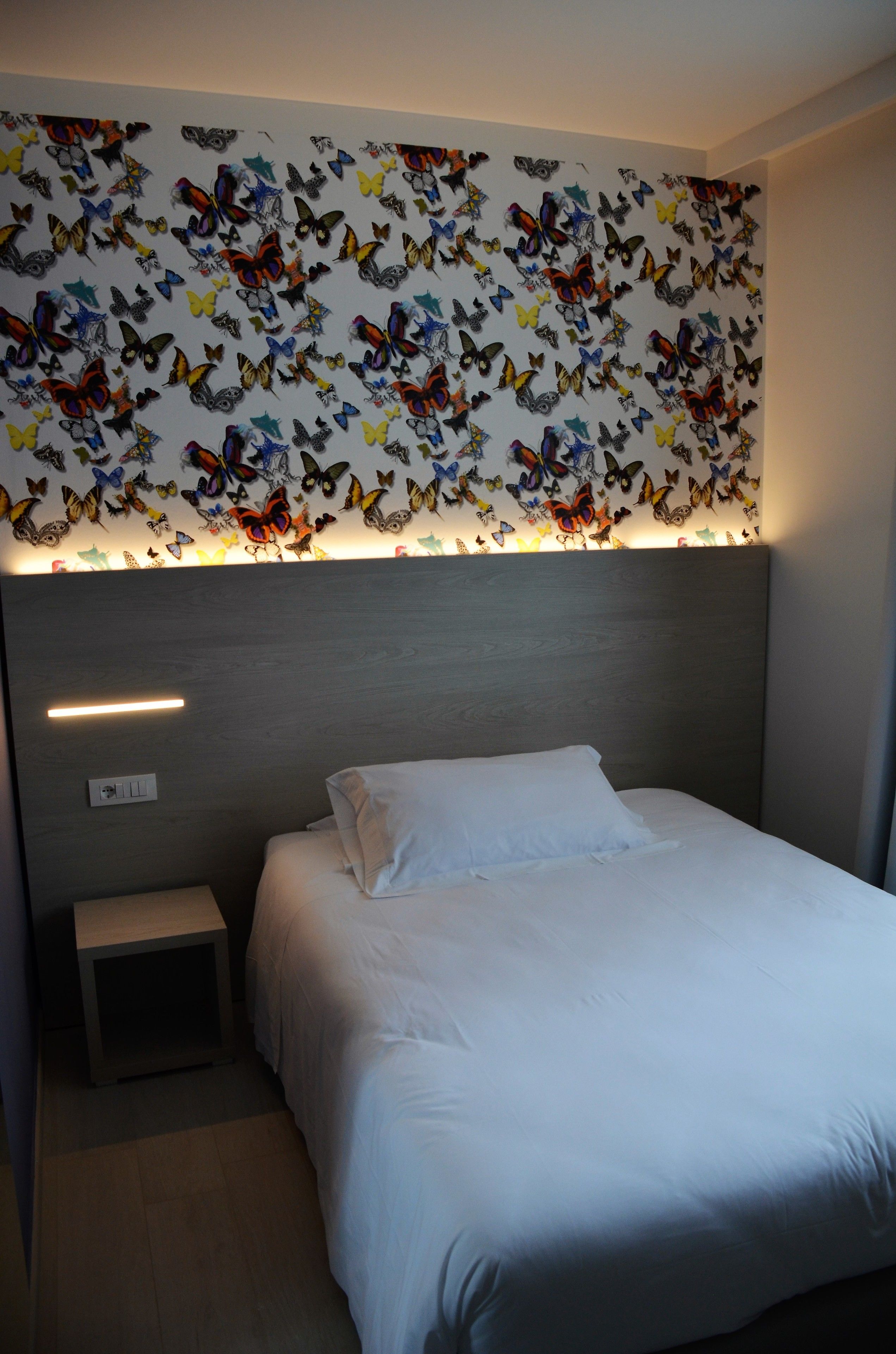 A bedroom with a bed, a nightstand, and a wall decorated with butterfly stickers.
