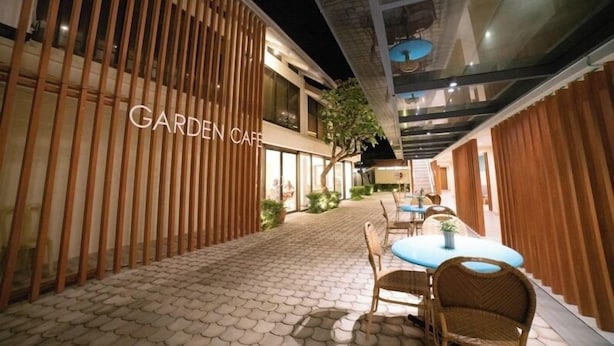Un café en un jardín con sendero de baldosas, separadores de madera y mobiliario de mimbre.