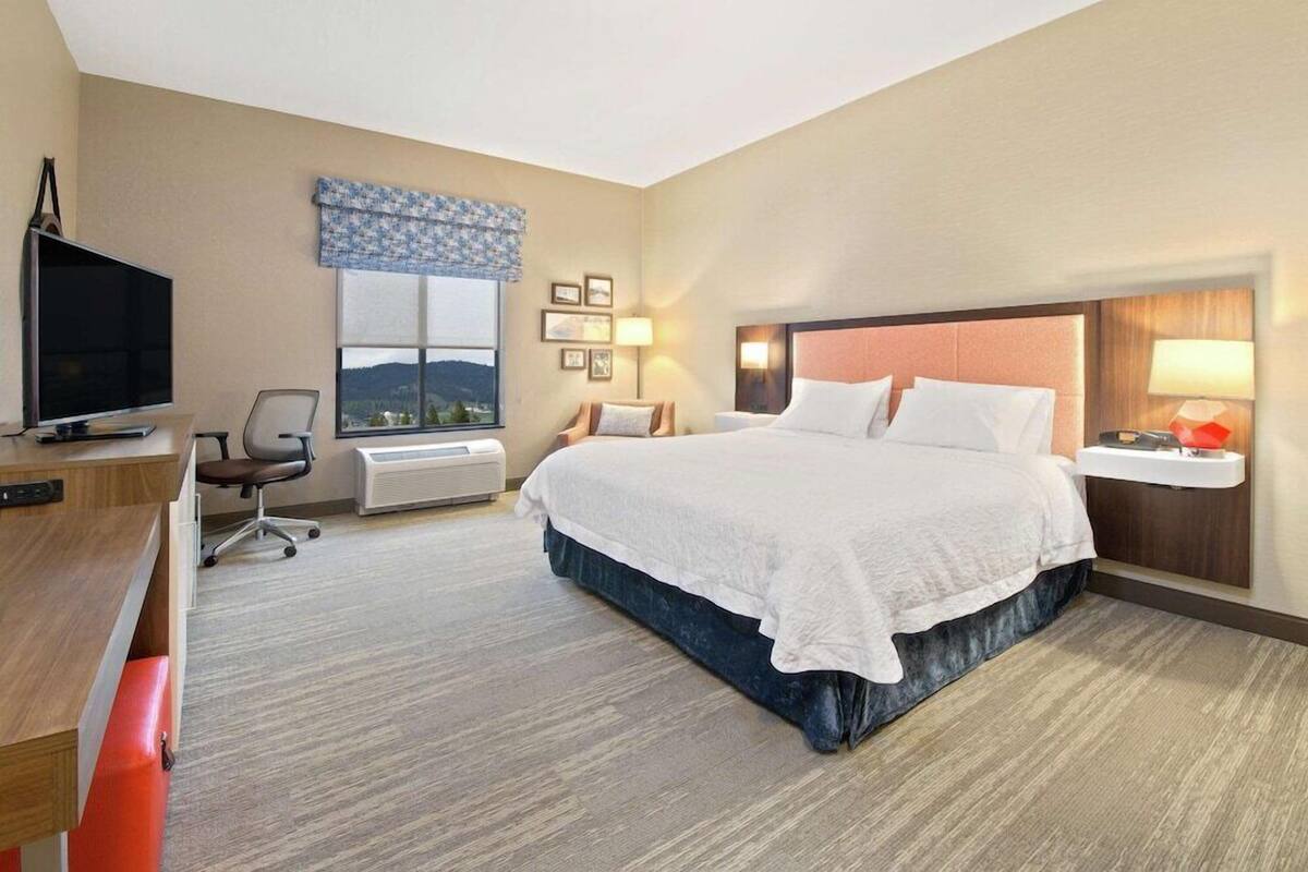 A hotel room with a bed, desk, chair, TV, window, and wall-mounted lamps.