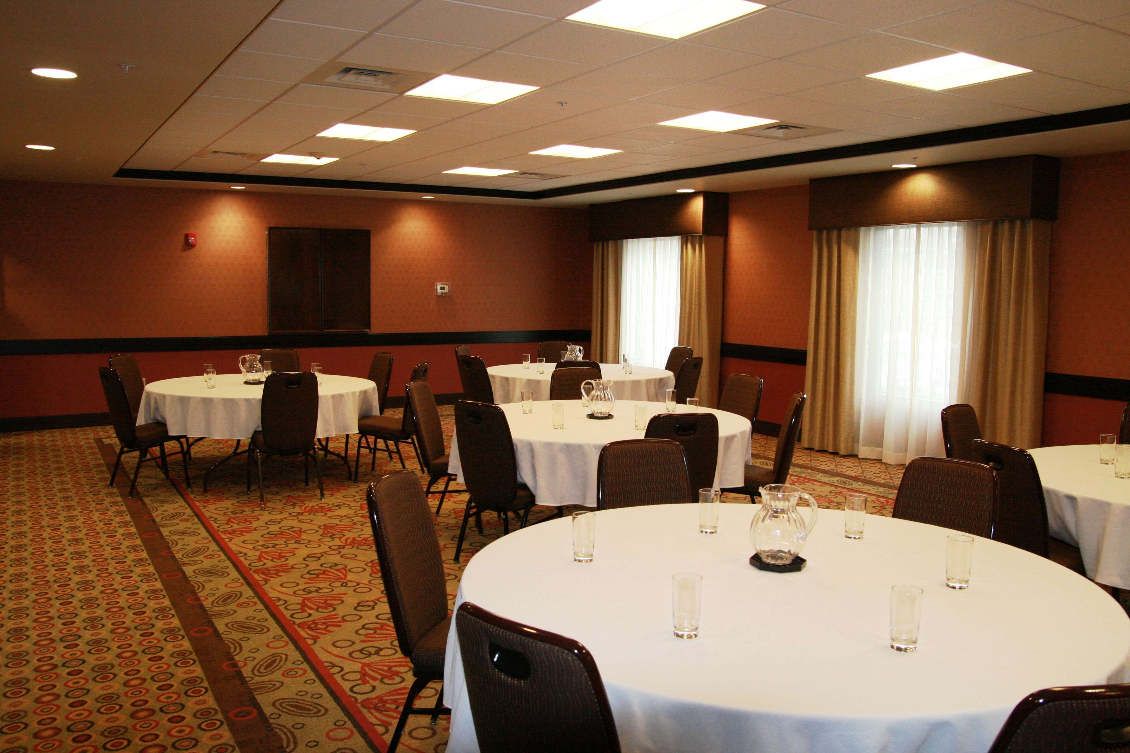 Une salle de conférence équipée de plusieurs tables rondes, chacune étant pourvue de chaises et de verres à eau.