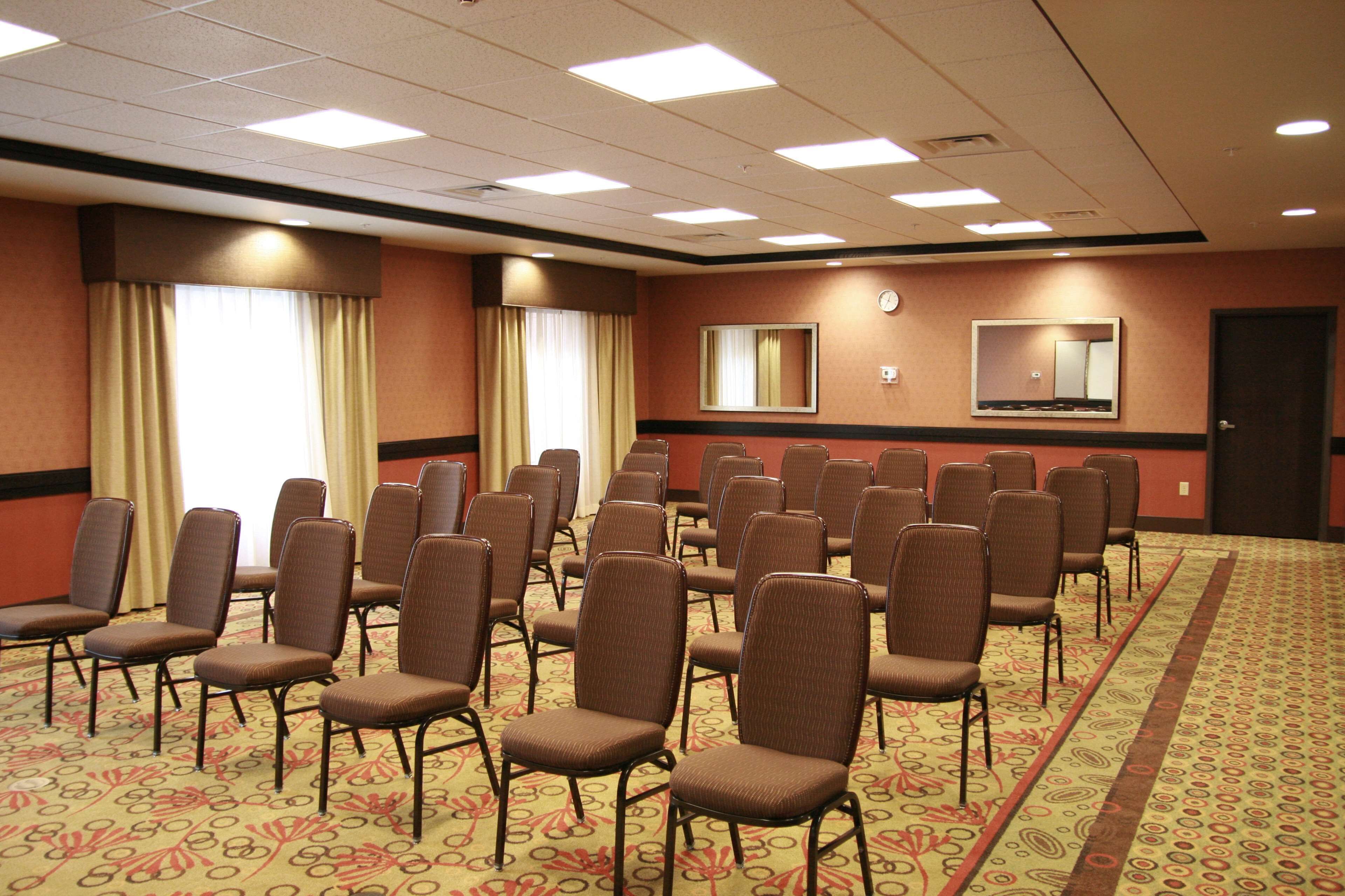 A conference room with rows of chairs, a carpeted floor, and a clock on the wall.