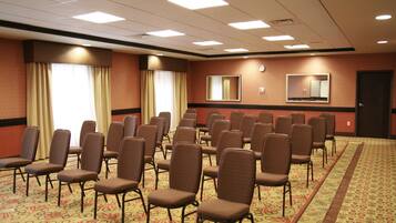 A conference room with rows of chairs, a carpeted floor, and a clock on the wall.