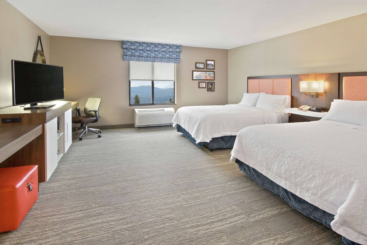 A hotel room with two beds, a desk with a television, a chair, and a window with a view.