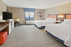 A hotel room with two beds, a desk with a television, a chair, and a window with a view.