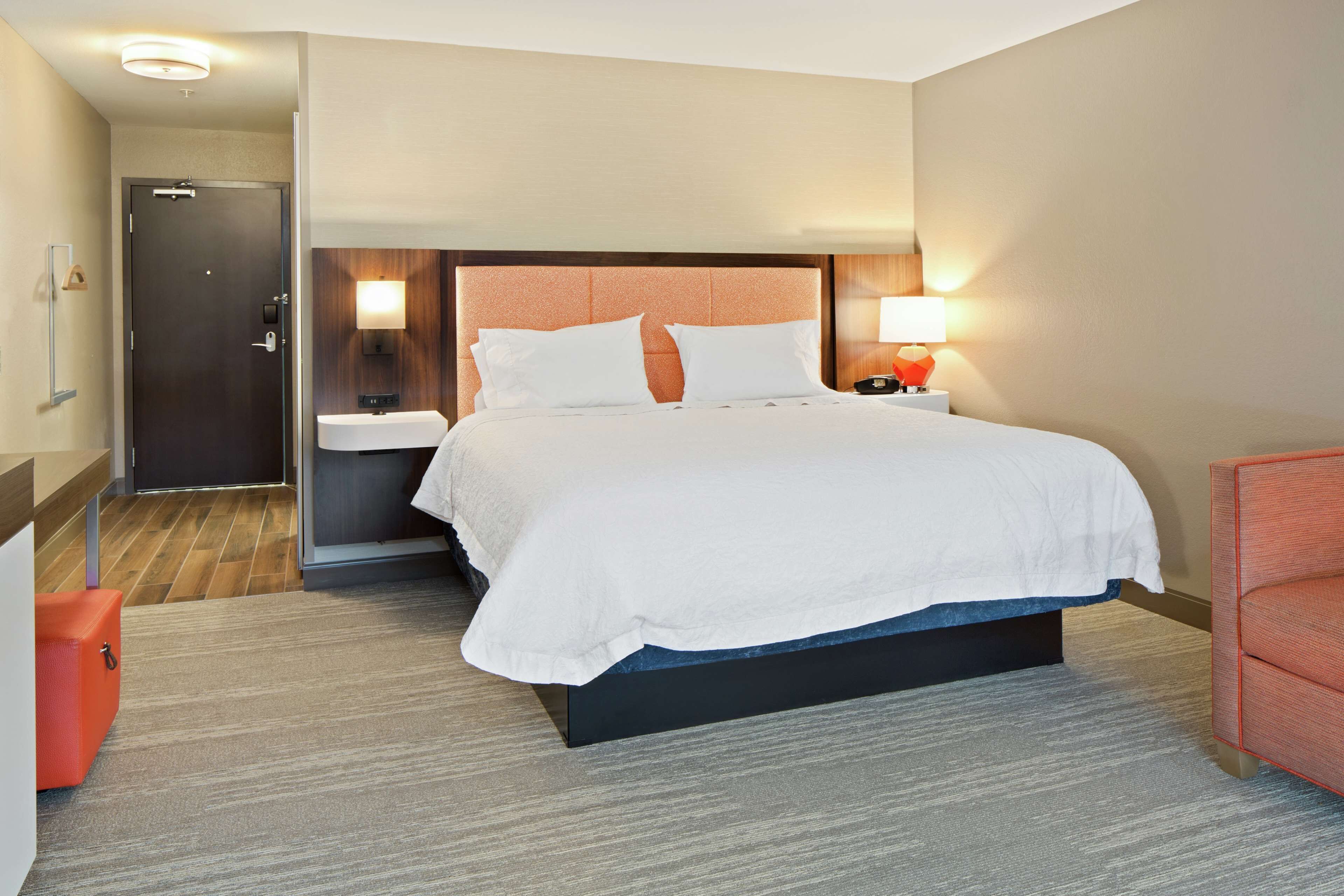 Ein Hotelzimmer mit Bett, Nachttisch, Lampe und einer Tür.