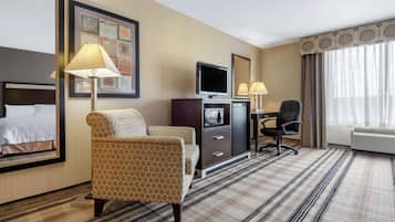 A hotel room with a bed, two armchairs, a desk with a TV, a mirror, and a window with curtains.