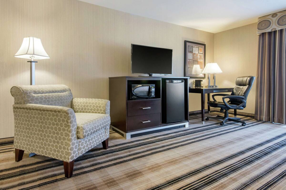 Una habitación de hotel con sofá, escritorio con computadora, televisión y microondas.