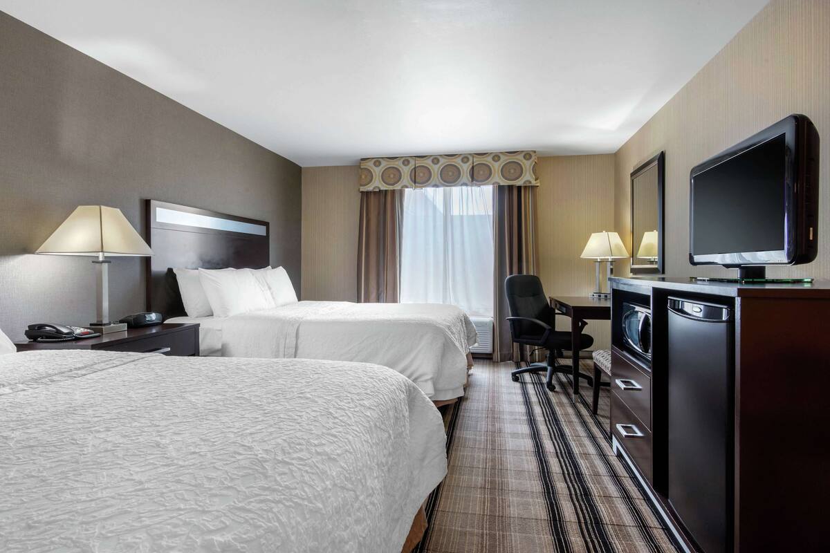 Habitación de hotel con dos camas, un escritorio con silla, televisión y minibar.